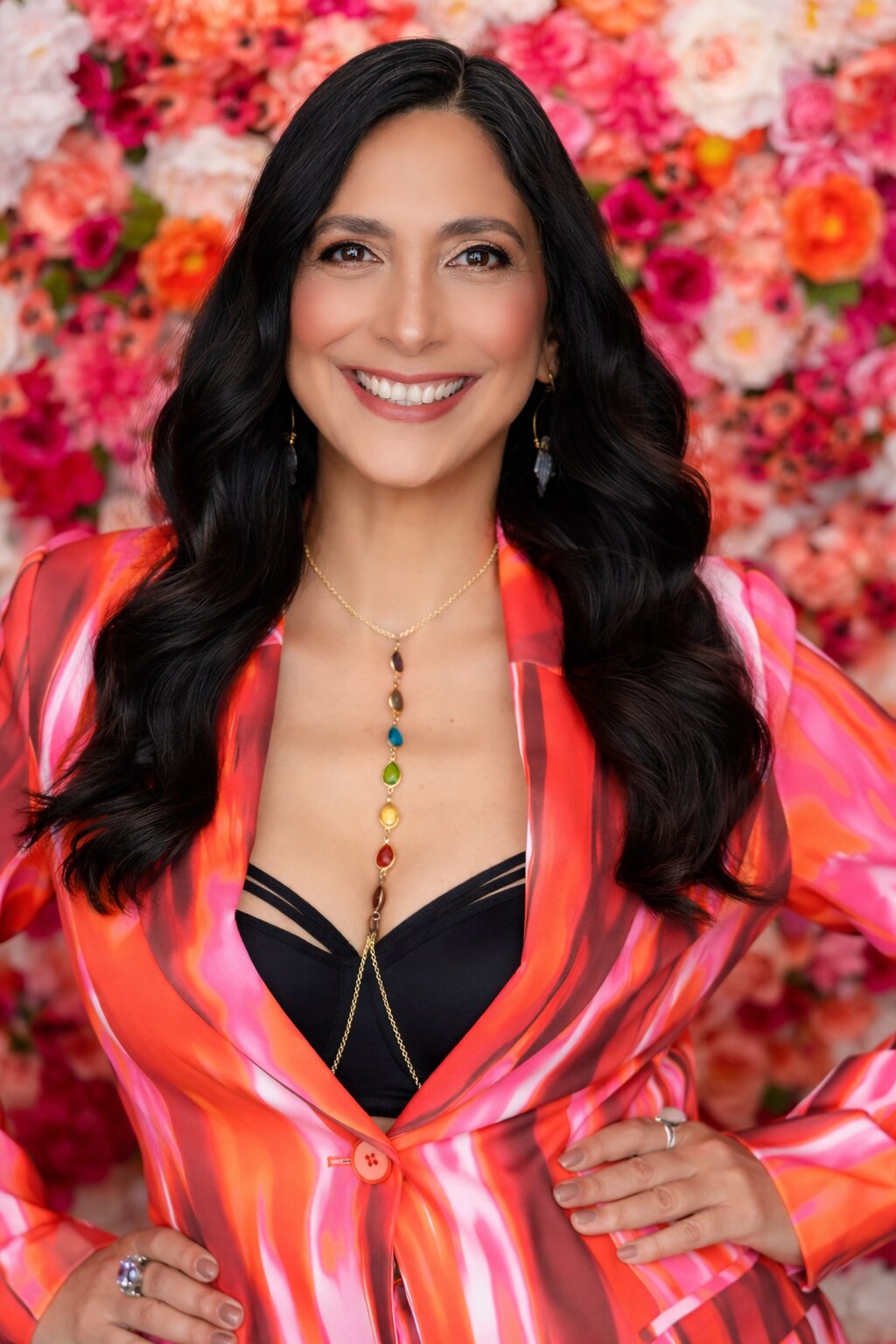 Kris Seraphine smiling in a vibrant pink and orange jacket before a wall of flowers